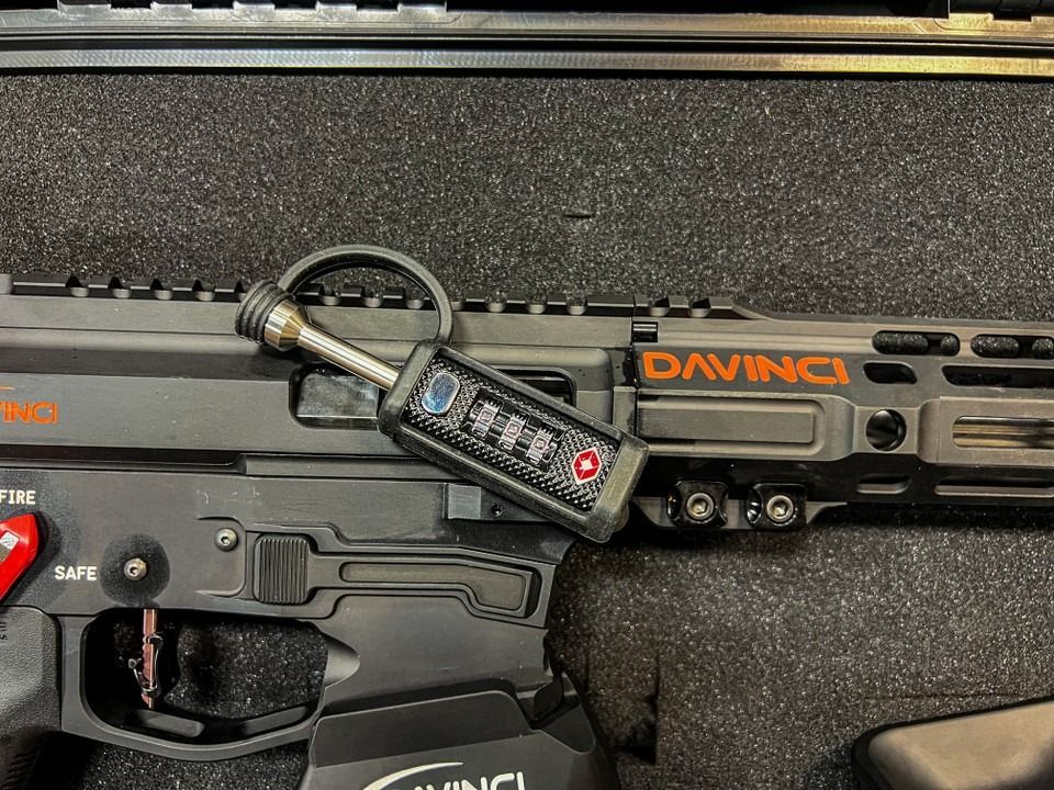 Black handgun with mounted laser and red toggle in a foam-lined case, labeled DA VINCI.
