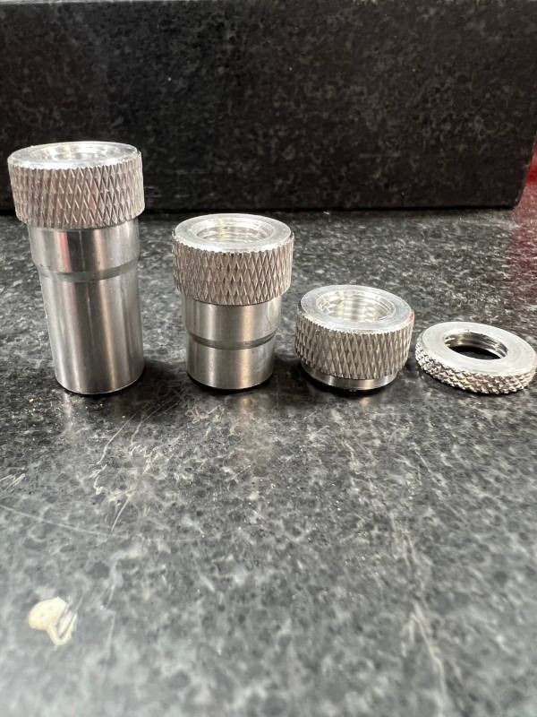 Four small silver metal knurled cylinders and a flat ring arranged on a dark countertop.