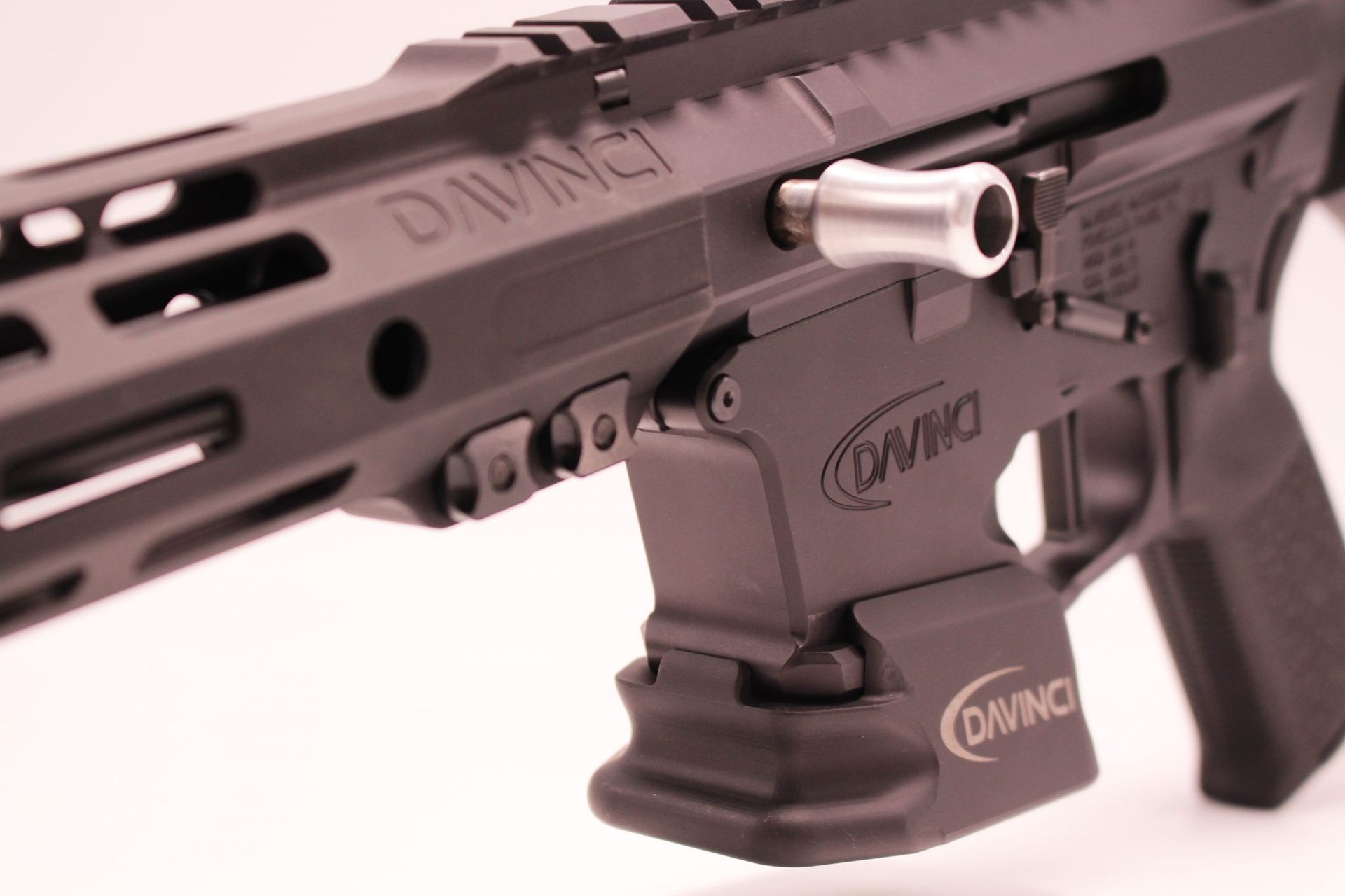Close-up of a black rifle mounted on a tactical accessory, with a pink-tinted background
