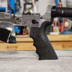 Close-up of a handgun in a workshop, showing a black grip and metallic frame on a bench.