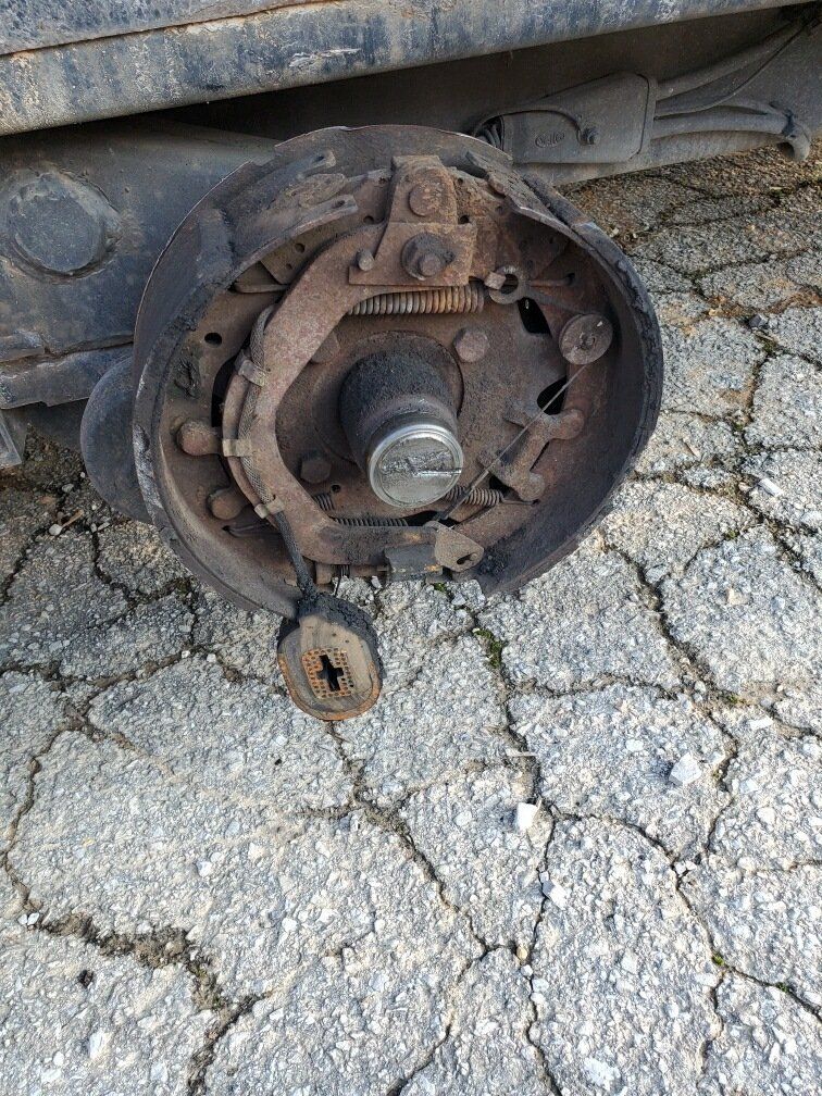 A broken brake caliper is sitting on the ground next to a car.