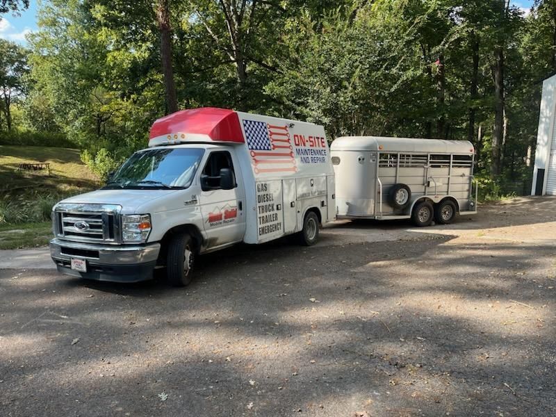 A white truck with an American flag on top is parked next to a horse trailer.