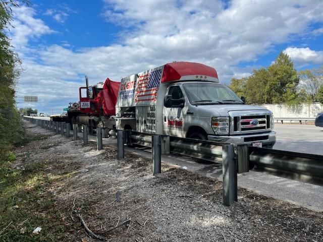 A white van is parked on the side of a highway next to a dump truck.