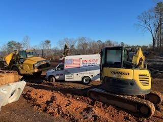 A yellow excavator is parked next to a white van on a dirt road.