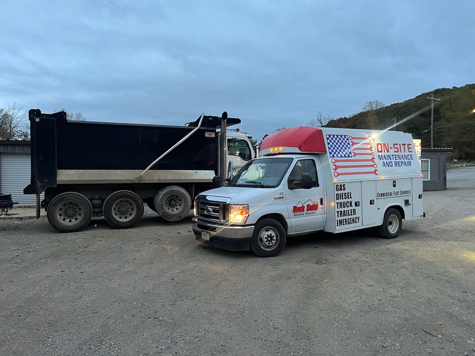 A white truck with an American flag on top is parked next to a dump truck.