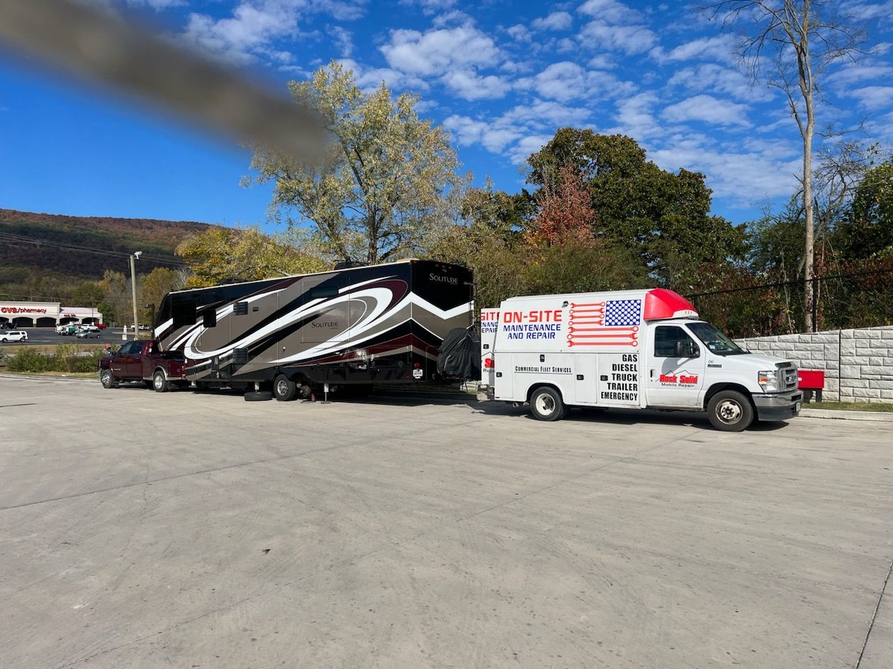 An RV is being towed by a truck and a white van.