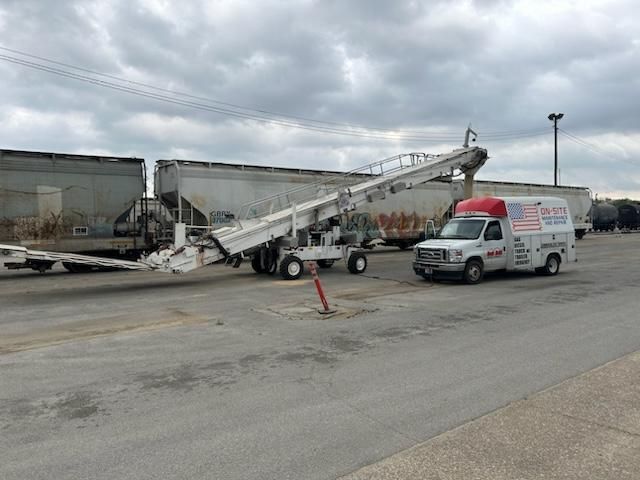 A white van is parked next to a conveyor belt in a parking lot.