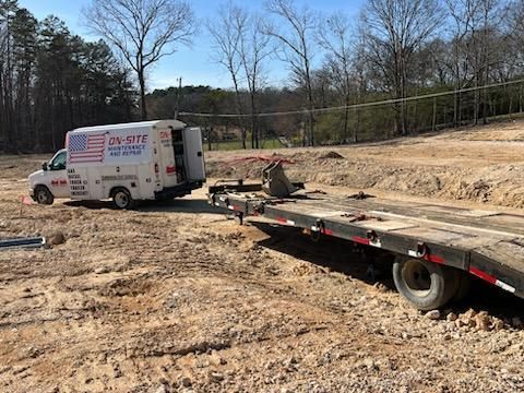 A white van is towing a flatbed truck in a dirt field.