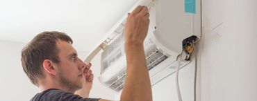 A man is installing an air conditioning unit on a white wall.