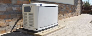 A white generator on a concrete pad next to a brick and stone wall.