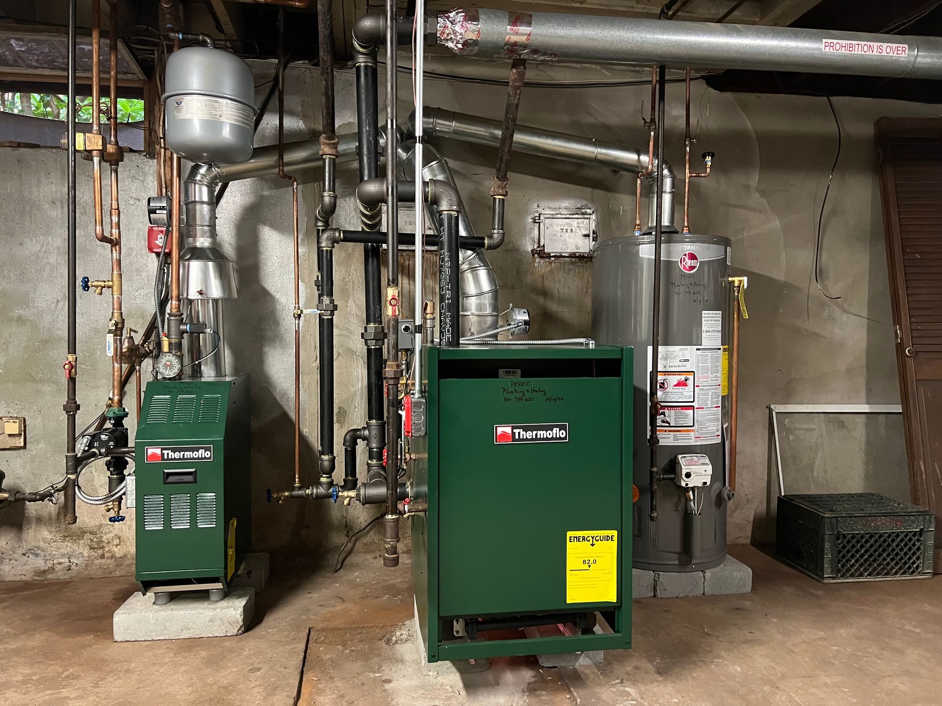 A green boiler is sitting in a basement next to a water heater.