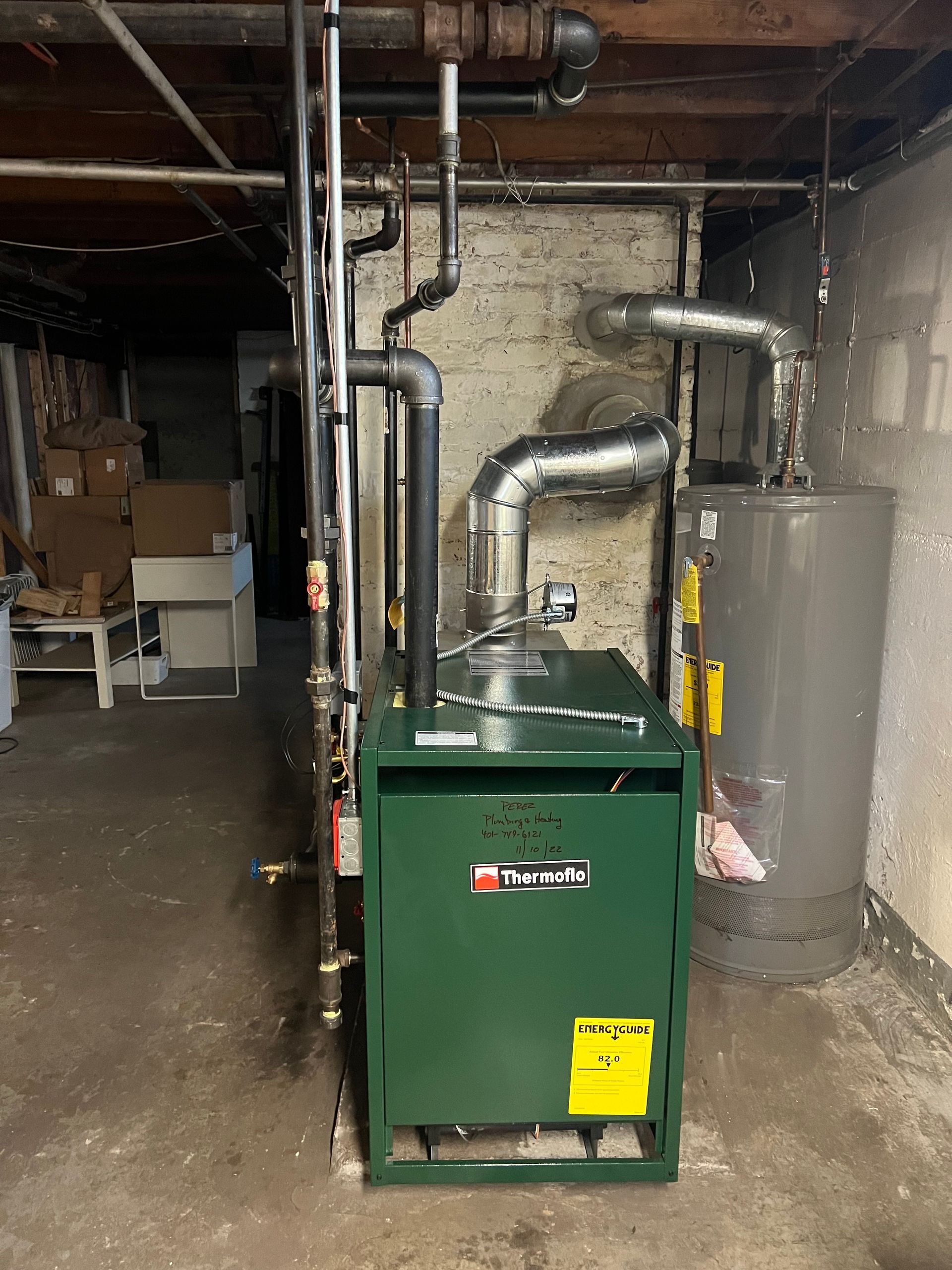 A green boiler is sitting in a basement next to a water heater.