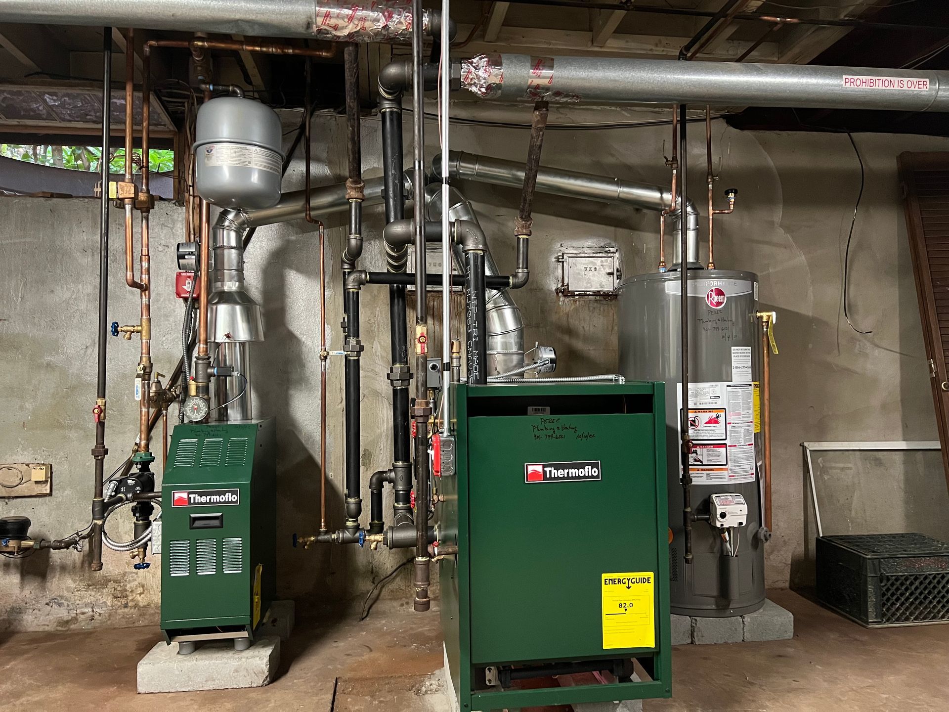 Two green boilers are sitting next to each other in a basement.