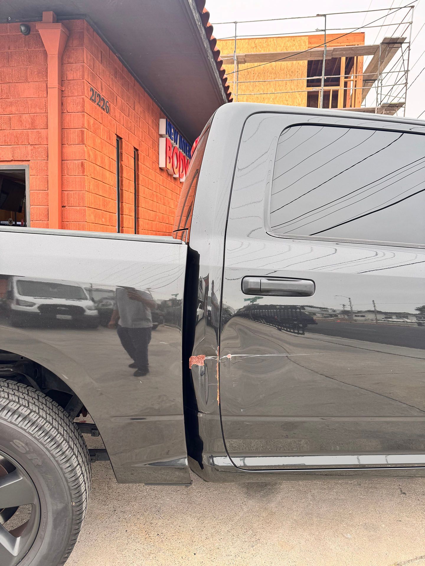 Black pickup truck parked outside a brick building, with a person reflected in the side.