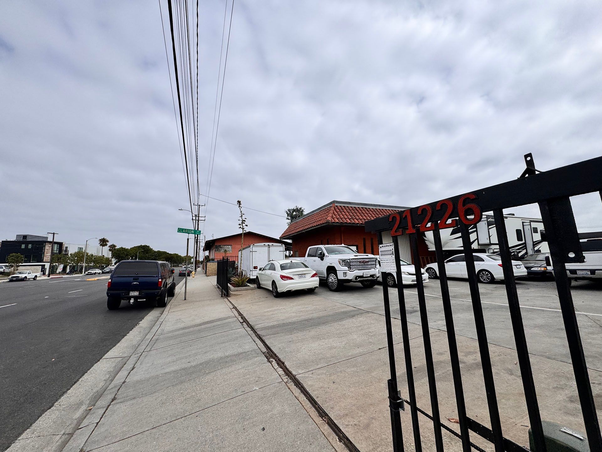 A street scene with a building and cars, cloudy sky. An open gate with numbers 