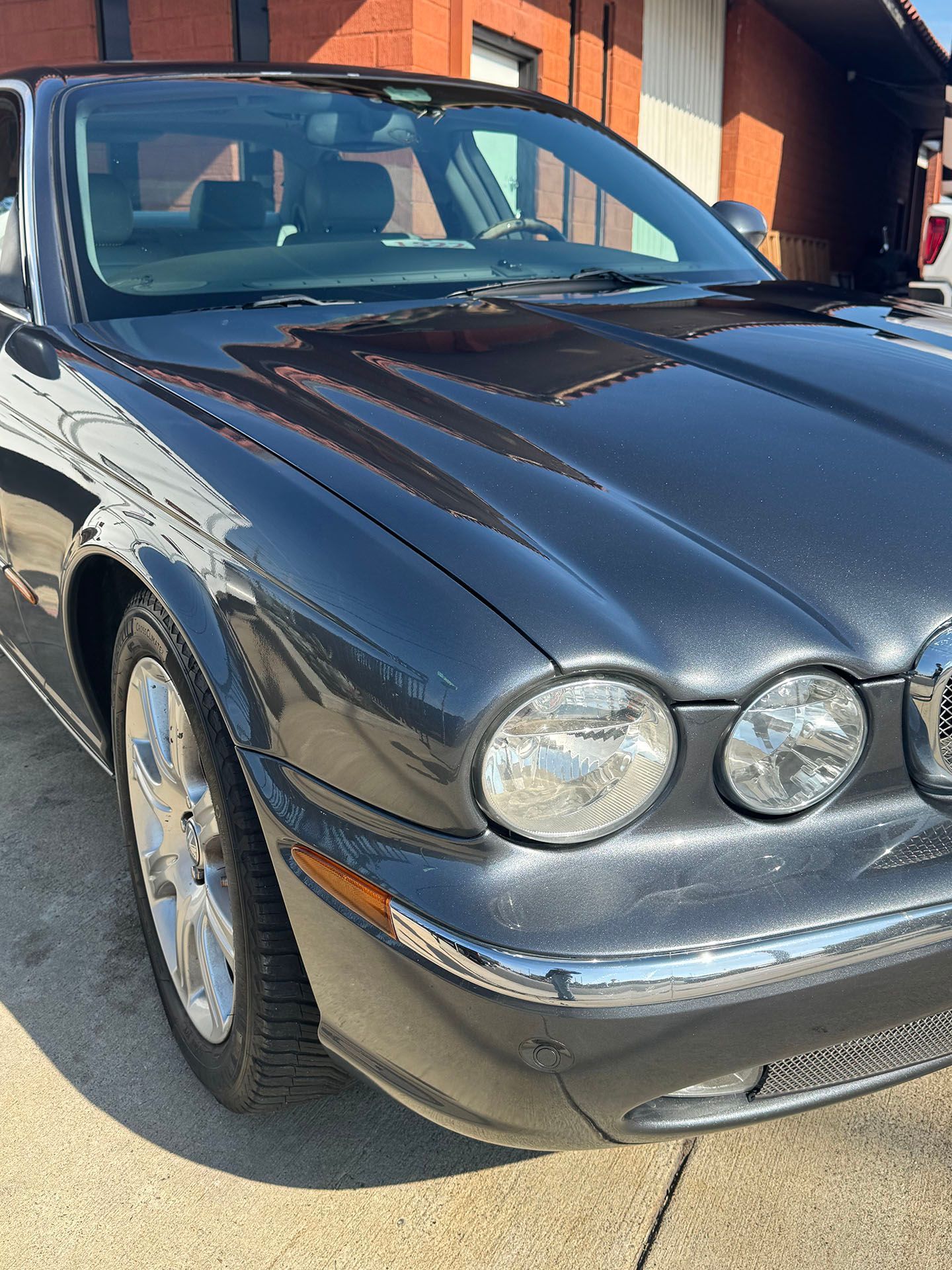 Dark gray Jaguar car parked outside; sunny day.