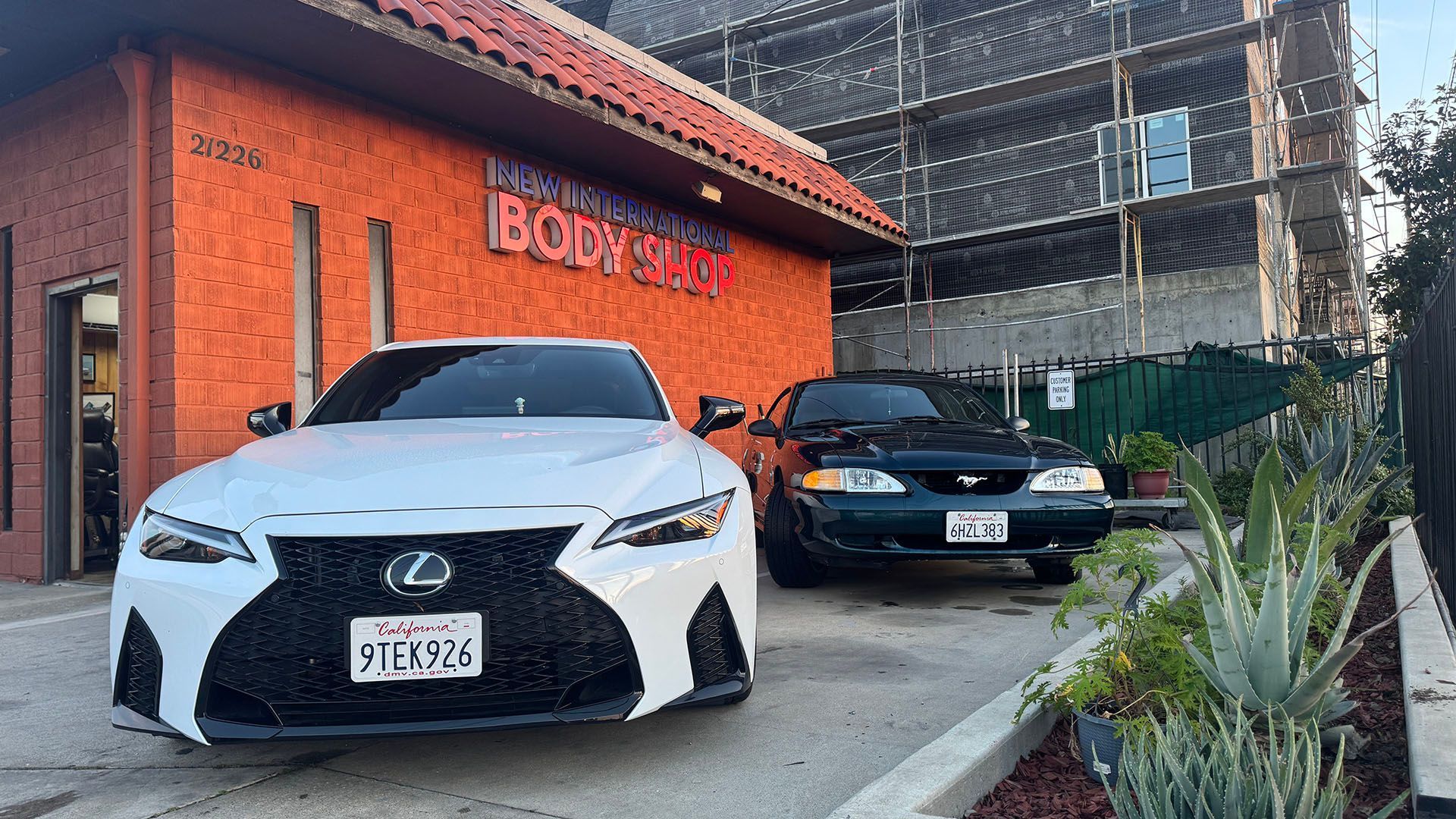 White Lexus and dark green Ford Mustang parked in front of a body shop.