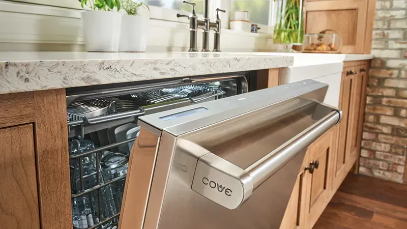 Stainless steel Cove dishwasher door opening in a modern kitchen with wooden cabinets and marble countertops.