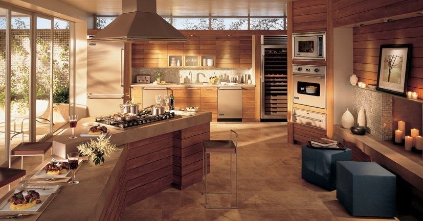 A modern, warm-toned kitchen with a wooden island, stainless steel appliances, and a dining area under natural light.