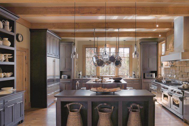 A spacious kitchen with dark cabinetry, a central island with woven baskets, and overhead beams and hanging cookware.