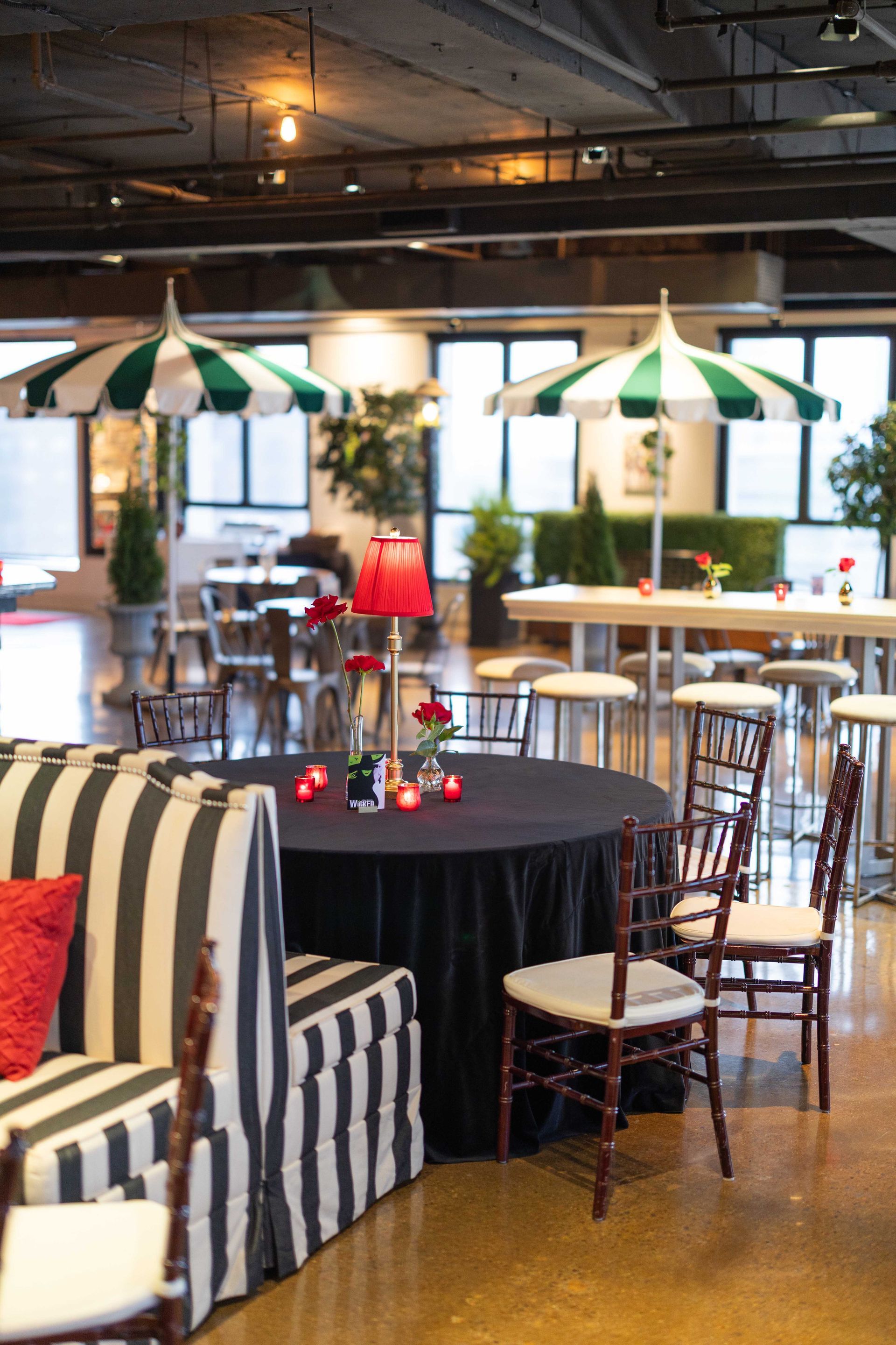 An elegant event space with a black and white striped sofa, round table set for guests, and green and white striped umbrellas.
