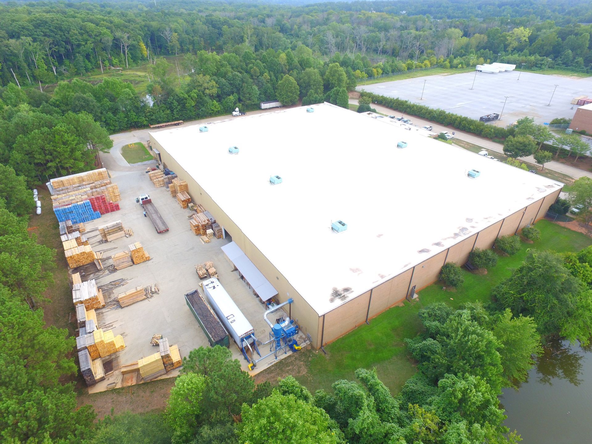 Aerial view of a large white warehouse beside a tree-lined road, with loading docks and parked trailers.