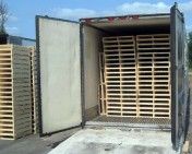A semi-trailer truck with open doors, loaded with stacks of light-colored wooden shipping pallets.