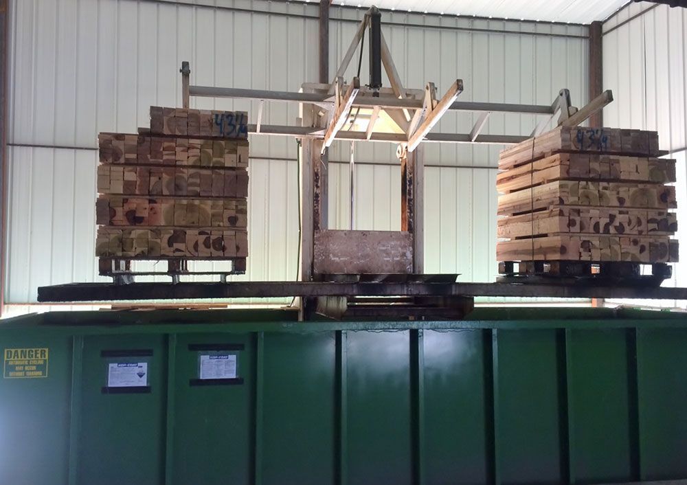 Two stacks of wooden boards on pallets sit on a heavy-duty green industrial machine in a workshop.
