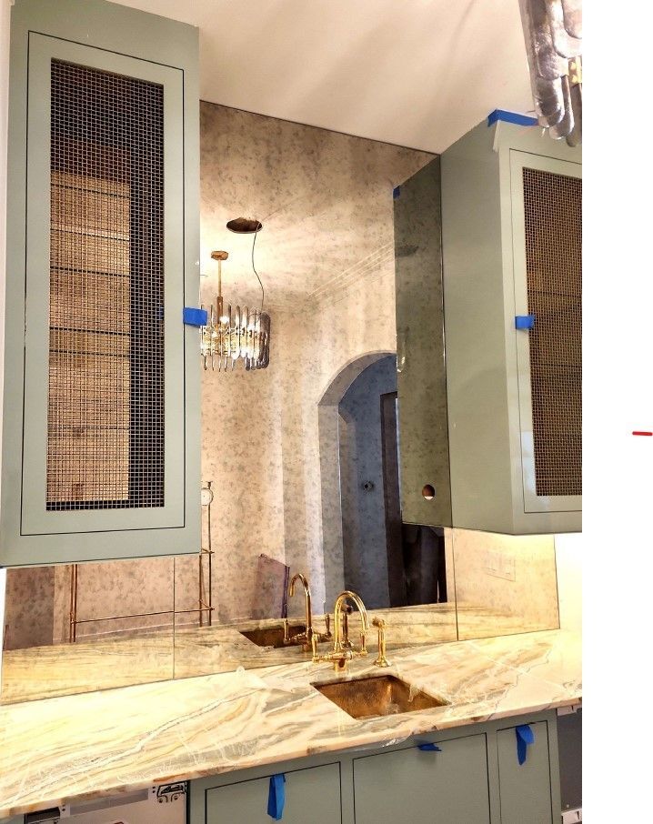 Sage green cabinets with wire mesh inserts, gold fixtures, and a marble countertop in a kitchen.