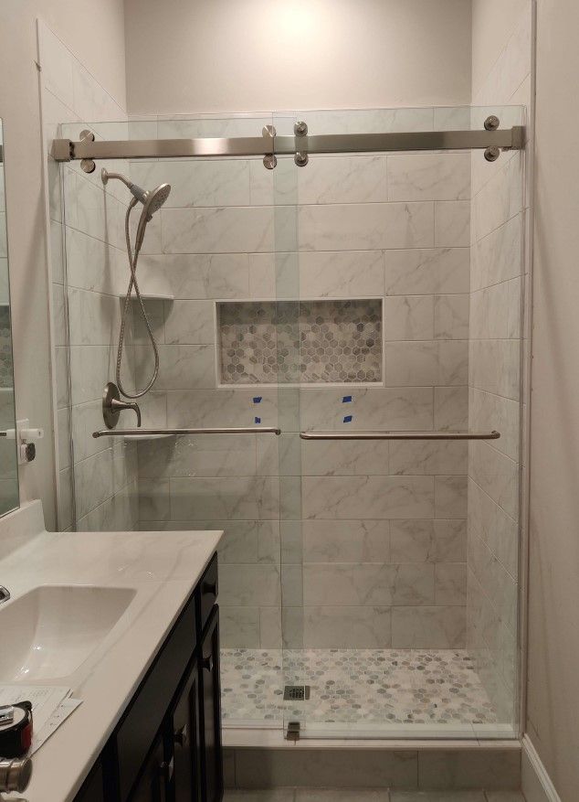 Modern shower with sliding glass doors, marble-look tile, and a pebble-stone shower floor.