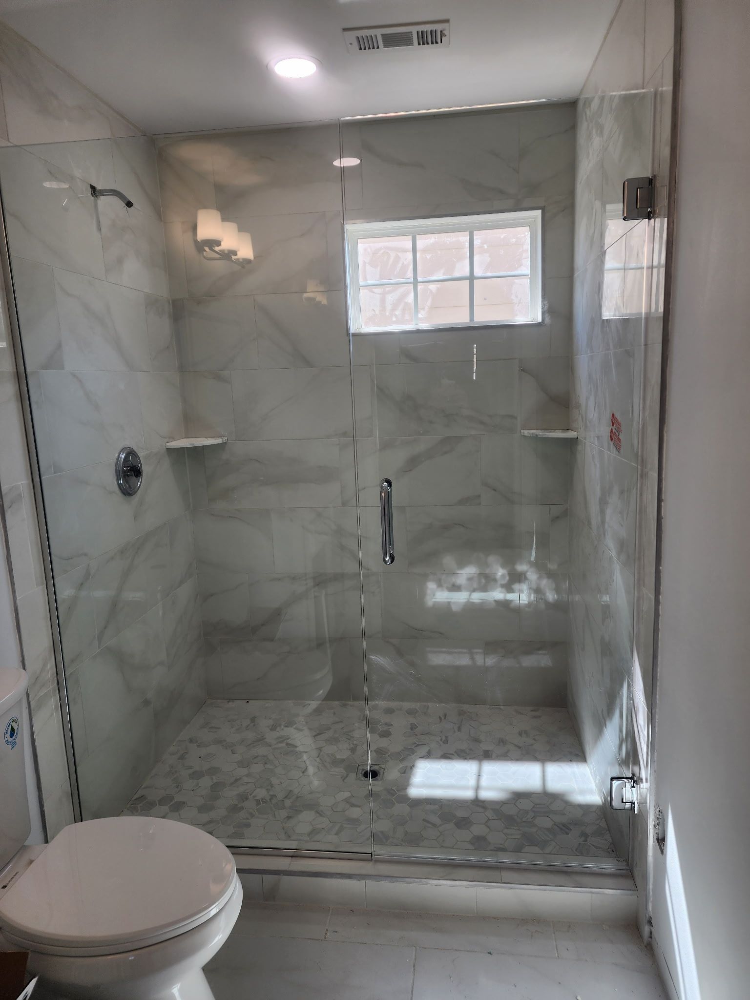 Modern bathroom with a glass shower, white marble tile, and a toilet.