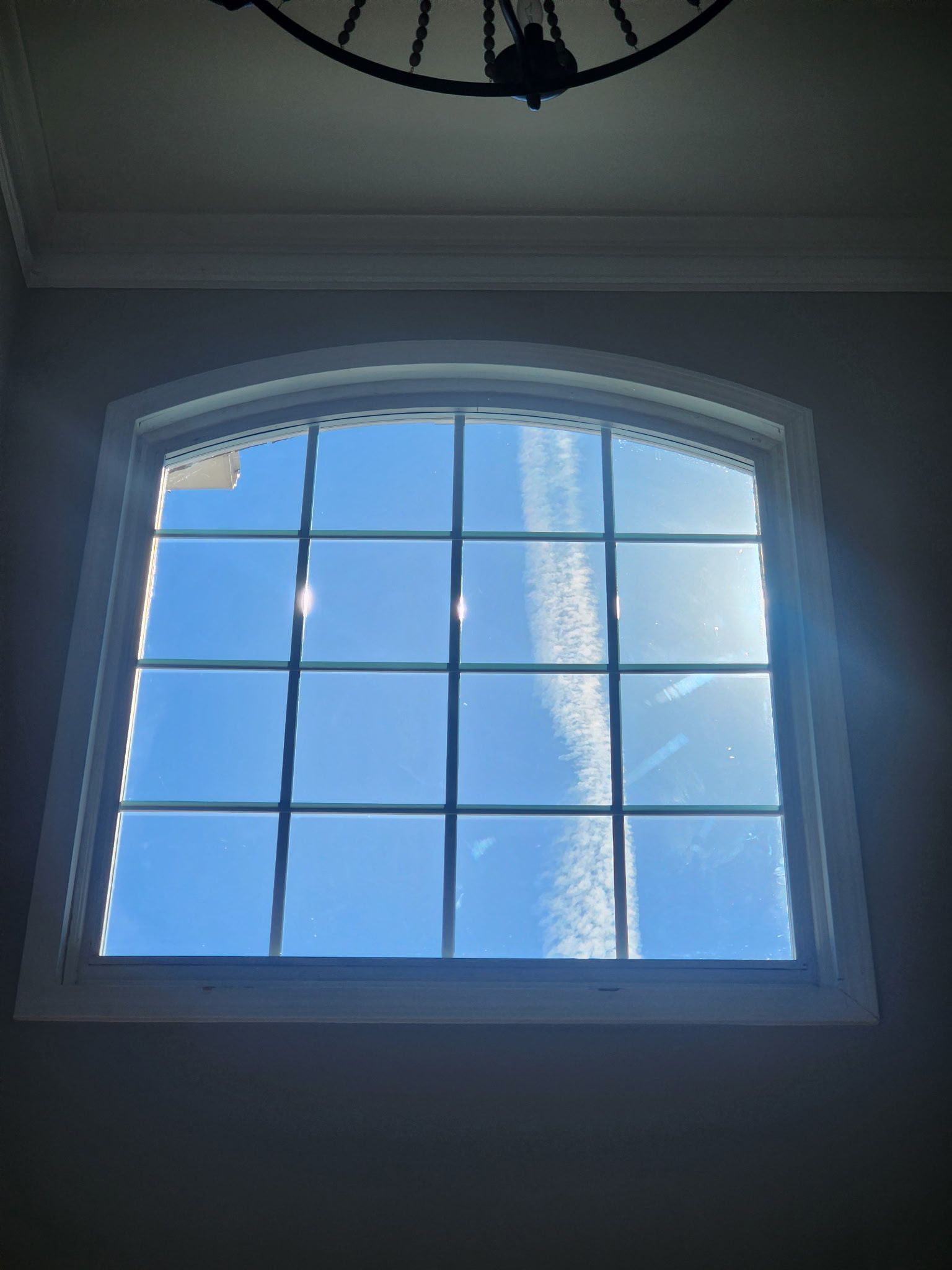 Window with white frame, paneled glass, and arched top. Blue sky and sunlight visible.