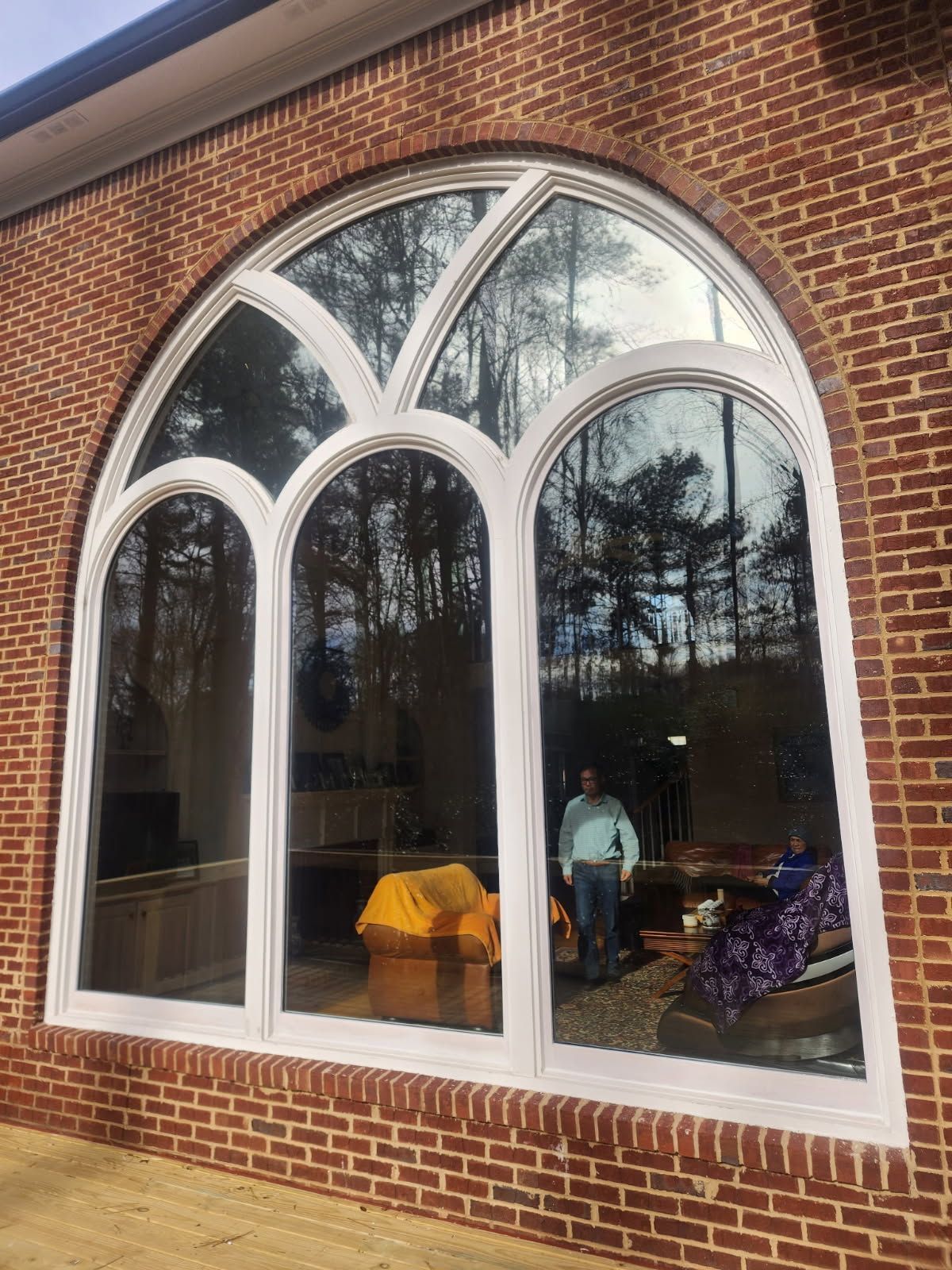 Large arched window with white trim in a brick building. Trees and person visible through the glass.