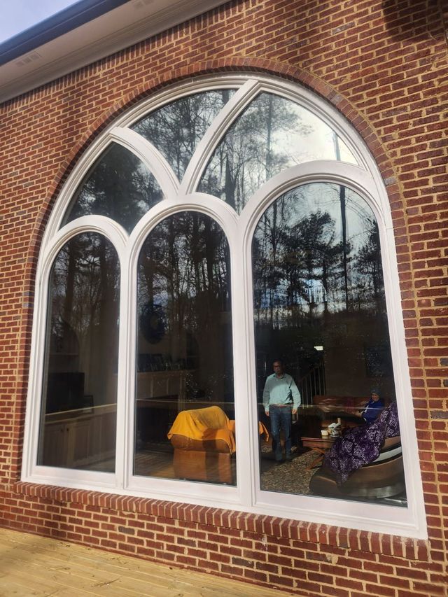 Large arched window with white trim in a brick building. Trees and person visible through the glass.