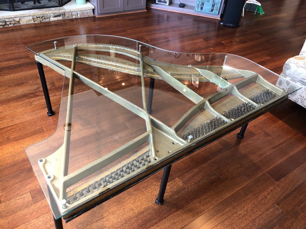 Piano-shaped coffee table with glass top; brown wooden floor in living room.