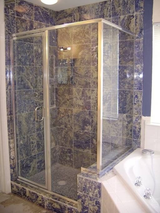 Shower stall with glass doors, blue marbled tile walls, and a tub nearby.