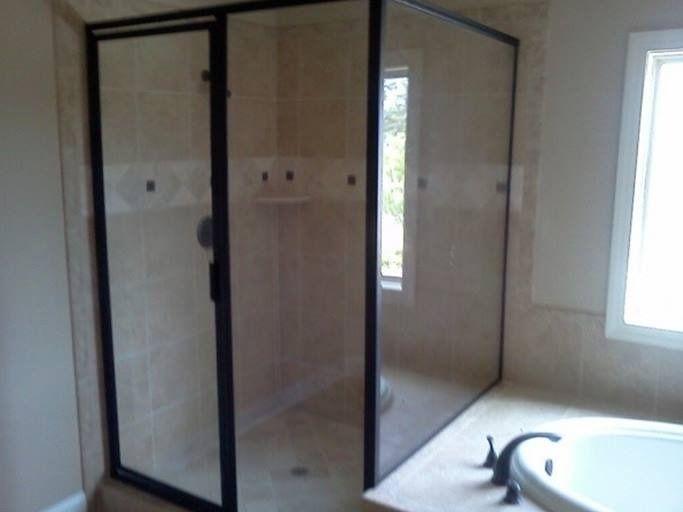 Shower enclosure with black framing, beige tile walls and floor, and a window.