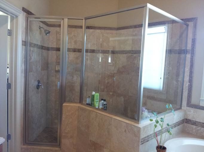 A corner shower with glass doors and beige tile, built into a bathroom with a window.