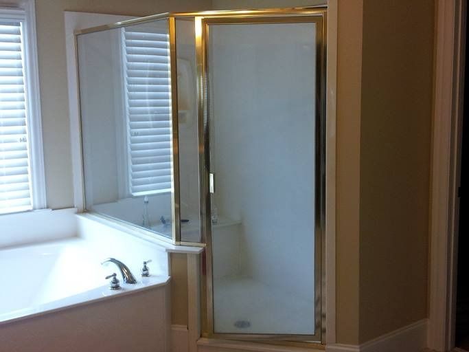 Bathroom with a bathtub, shower with frosted glass door, and gold trim.  Windows with blinds are on the left.