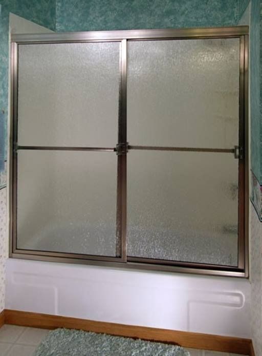 Sliding glass shower doors with frosted glass panels, over a white bathtub.