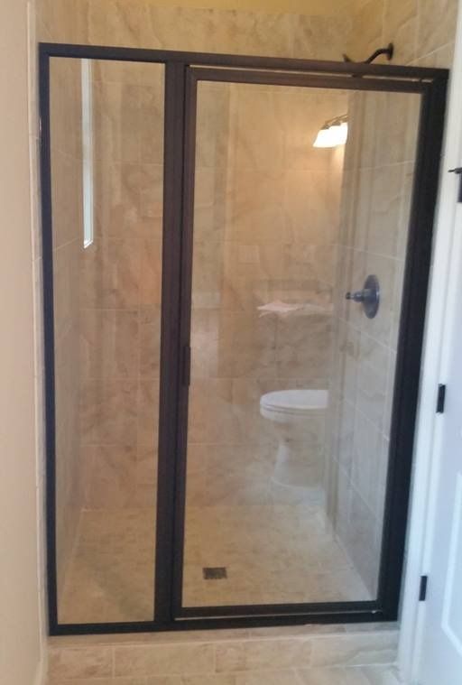 Shower with black framed glass doors, light beige tile.  Bathroom setting.