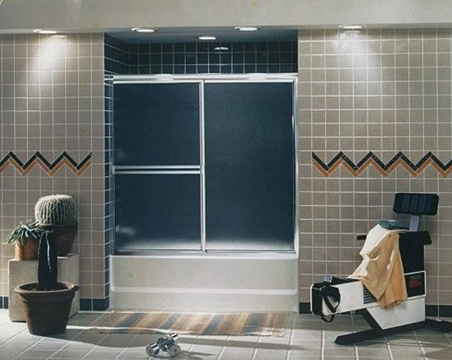 Bathroom with beige tile, shower, and a chair.