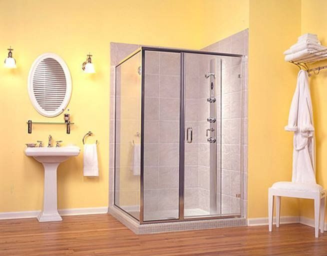 Bathroom with yellow walls, a glass shower, a pedestal sink, and a white chair.