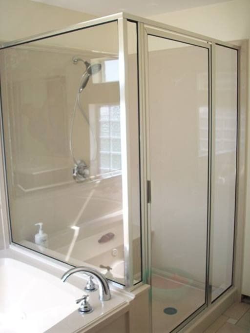 A clear glass shower enclosure next to a bathtub, with chrome fixtures and a window.