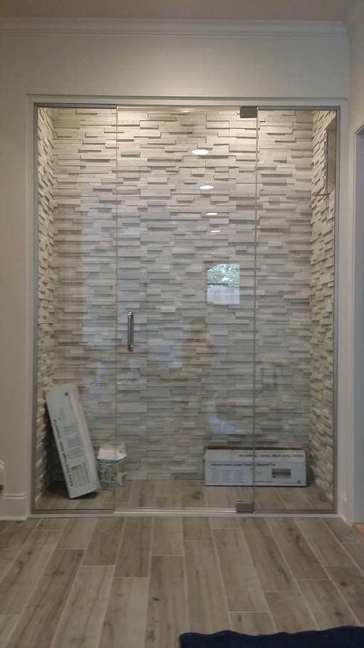A glass shower enclosure with a stone tile back wall, and some items on the floor.