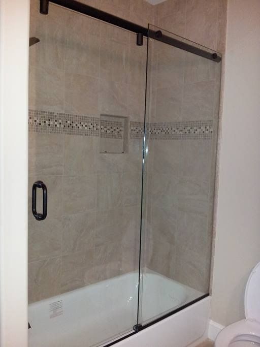 Shower with a sliding glass door and dark metal frame, set in a tiled alcove with a built-in shelf.