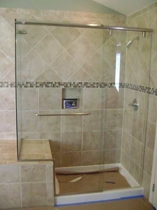 A tiled walk-in shower with a glass door, seat, and silver fixtures.
