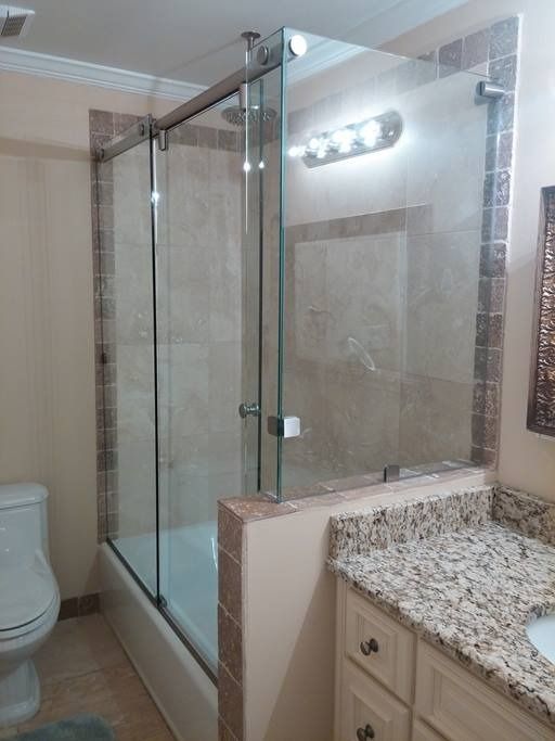 Glass shower enclosure with sliding door in a bathroom. Beige and brown tiles surround the shower.