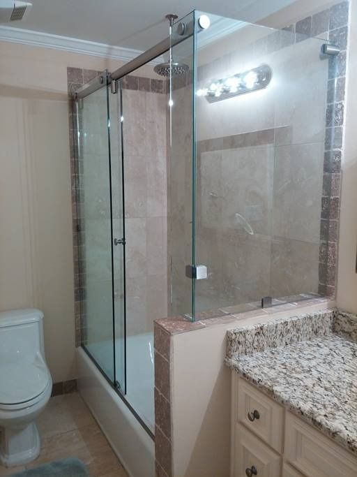Bathroom with glass shower doors, granite countertop, beige tiles, and white toilet and vanity.