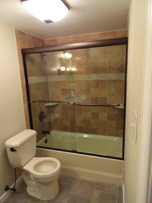 Bathroom with toilet, tub, and shower with brown tile and sliding glass doors.